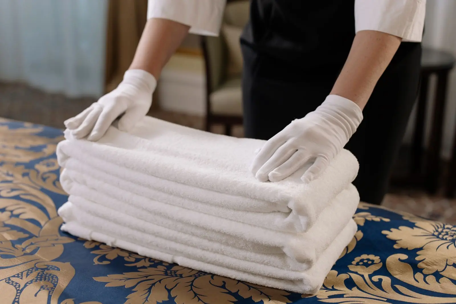 Housekeeper setting a stack of folded white towels down on a freshly made bed